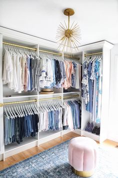 a walk in closet with clothes on hangers and a rug underneath the chandelier