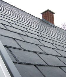 the roof of a house with slate shingles on it and a chimney in the background