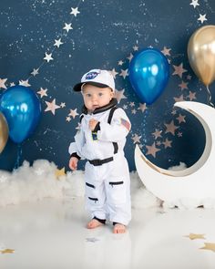 a little boy dressed in an astronaut suit standing next to blue balloons and gold stars