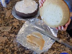 a person holding a piece of bread in front of two cakes on tin foil and a knife