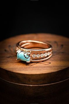 two gold rings sitting on top of a wooden box next to a turquoise stone and diamond ring