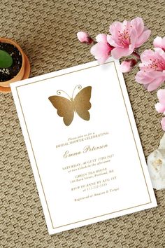 a white and gold wedding card with a butterfly on it next to some pink flowers