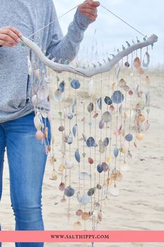 a woman holding a mobile made out of seashells on the beach with text overlay