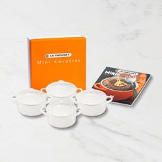 the mini cookware set is next to an orange book and white dishes on a marble countertop