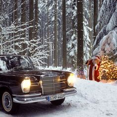 an old fashioned car is parked in the snow near a christmas tree with lights on it