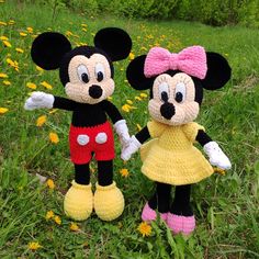 two crocheted mickey and minnie mouse dolls standing in the grass with dandelions