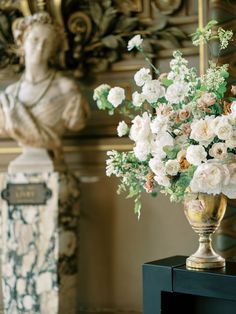 a vase filled with white flowers sitting on top of a table next to a statue