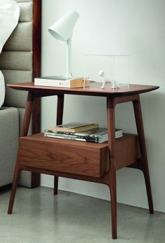 a wooden table with books and a lamp on it next to a couch in a living room