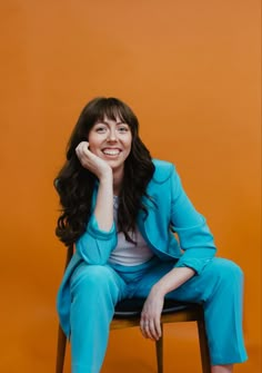 a woman sitting in a chair with her hand on her chin and smiling at the camera