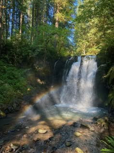 a waterfall with a rainbow in the middle of it and lots of trees around it