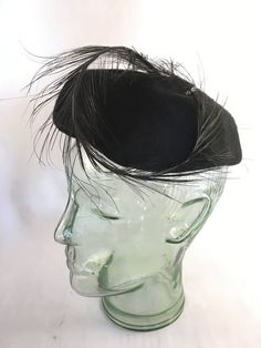 "This is a simple, but elegant black hat with a wonderfully swooped black feather perched on it! The feather is attached in the back with a decorative bow, and gracefully curls to the left side of the hat, with a rhinestone bead holding it in place. This hat is in excellent vintage condition, is clean & ready to wear.  Measures 6.5\" wide." Black Fitted Flat Cap Felt Hat, Black Flat Cap For Party, Elegant Black Feather Trim Costume Hat, Elegant Black Costume Hat With Feather Trim, Adjustable Black Feathered Headpiece, Adjustable Black Feather Headpiece, Elegant Black Fascinator With Feather Trim, Elegant Flat Cap For Party, Adjustable Feathered Top Hat For Evening