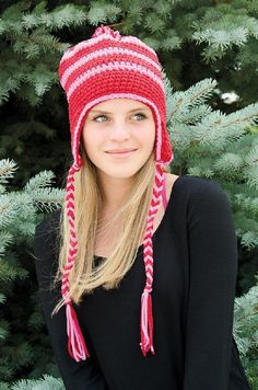 a woman wearing a red and white knitted hat standing in front of pine trees