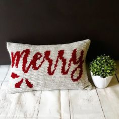 a pillow with the word merry on it next to a potted plant