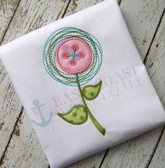 a pink flower with green leaves is embroidered onto a white fabric napkin on a wooden surface