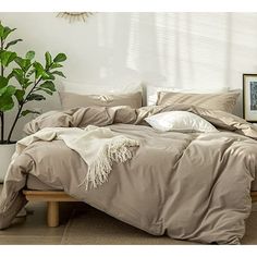 an unmade bed in a white room with potted plants