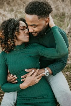 a man and woman hugging each other in front of some tall grass with their arms around one another