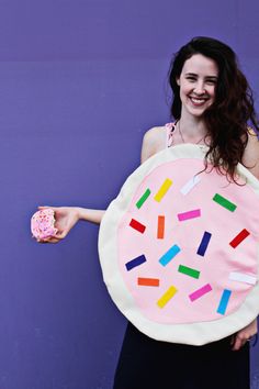 a woman holding a donut with sprinkles painted on it and wearing a pink apron