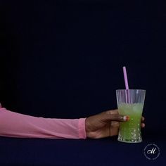 a woman holding a green drink in her hand with a pink shirt and blue nail polish