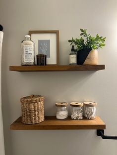 two wooden shelves above a toilet in a bathroom with towels and other items on the shelf