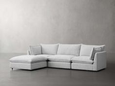 a white sectional couch with pillows on the top and bottom corner, in front of a gray wall