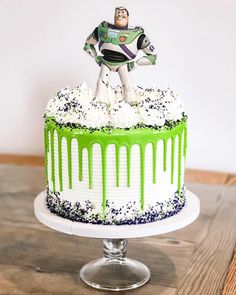 a green and white frosted cake with a toy buzz lightyear figure on top