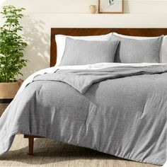 a bed with grey sheets and pillows in a room next to a potted plant