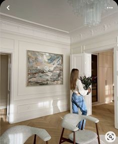 a woman standing in an empty room with two chairs and a painting on the wall