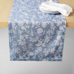 a blue table cloth with white flowers and leaves on it sitting on a wooden table