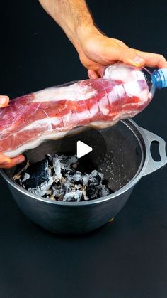 a person holding a large piece of meat in a pot with coals and water