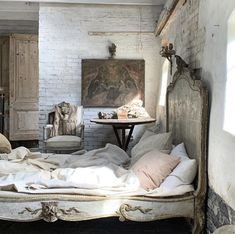 an old fashioned bed with white linens in a rustic style bedroom, next to a painting on the wall