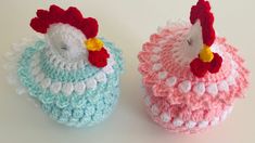 two crocheted chickens sitting next to each other on top of a white table