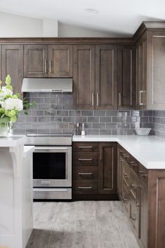 a kitchen with wooden cabinets and white counter tops, gray tile backsplash and stainless steel appliances