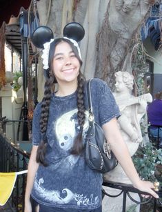 a girl with long braids and mickey mouse ears on her head standing in front of a statue