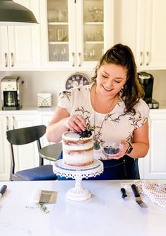 a woman standing in front of a cake on top of a white table with utensils