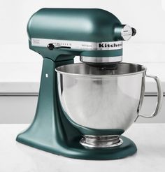 a green kitchen aid mixer sitting on top of a white counter next to a window