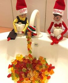 two elfs sitting on top of a sink filled with gummy bears