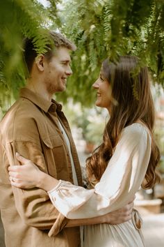 a man and woman standing next to each other under a green leafy tree together