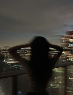 a woman standing on top of a tall building next to a city at night with buildings in the background