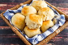 a basket filled with rolls sitting on top of a wooden table next to a blue and white checkered napkin