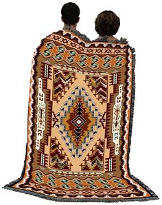 two people sitting on top of a rug with an orange and brown design in the middle