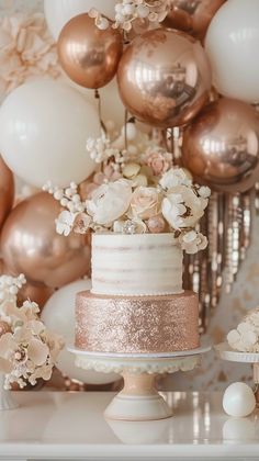 a wedding cake with gold and white flowers on top sits in front of some balloons