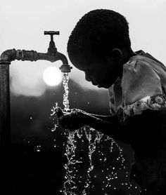 a little boy that is standing in front of a faucet with water coming out of it