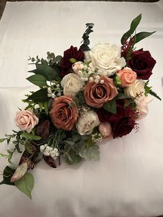 a bouquet of flowers sitting on top of a white cloth covered tablecloth with leaves