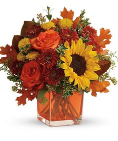 an autumn bouquet with sunflowers, roses and leaves in a square glass vase