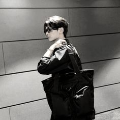 a woman standing in front of a wall with a black bag on her shoulder and sunglasses on