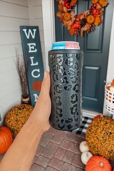 a person holding up a can in front of a door with pumpkins and other decorations