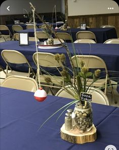 there is a vase with plants in it on the table at this function, which is decorated with blue tables cloths and white chairs