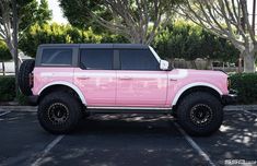 a pink truck parked in a parking lot next to some trees and bushes with black tires