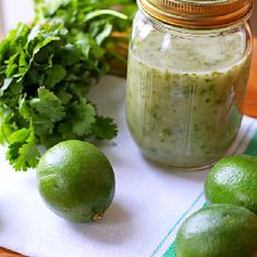 limes, cilantro and parsley sit on a table next to a jar of pesto