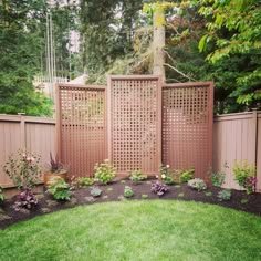 a garden with green grass and flowers next to a wooden privacy fence in the middle of a yard